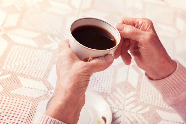 Une femme âgée boit du thé à la maison. Femme âgée tenant une tasse de thé dans leurs mains à proximité de la table. Vue horizontale du dessus — Photo