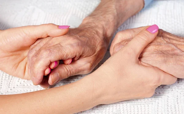 Old and young holding hands on light background, closeup. Care is at home of elderly — Stock Photo, Image