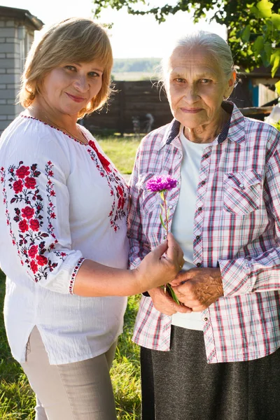 Medelålders kvinna kramar hennes mor i naturen. De riktiga känslorna av lycka. Mors dag. — Stockfoto