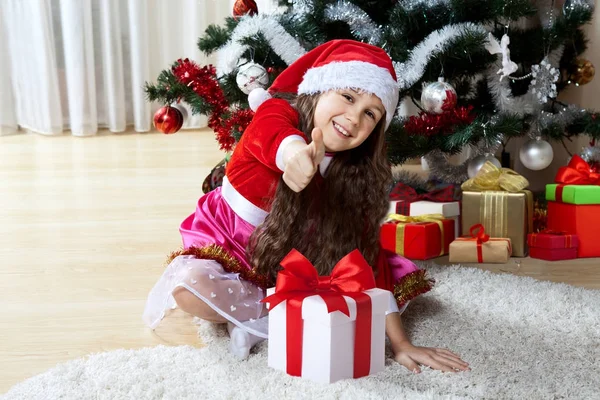 庆祝圣诞节、寒假和人们的概念。快乐的女孩与礼物在箱子里坐在装饰的圣诞树附近在家 免版税图库照片