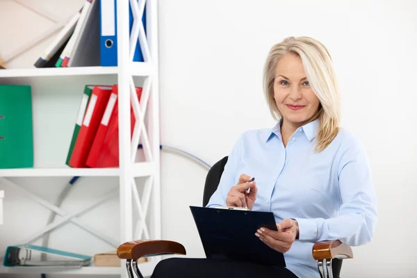 Zakenvrouw in kantoor met documenten werken. Mooie midden leeftijd vrouw op zoek naar camera met glimlach terwijl aanbrengen in het kantoor. — Stockfoto
