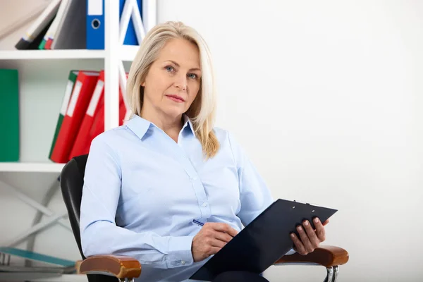 Affärskvinna arbetande i kontor med dokument. Vackra mellersta år kvinna som tittar på kamera med leende medan placering i office. — Stockfoto