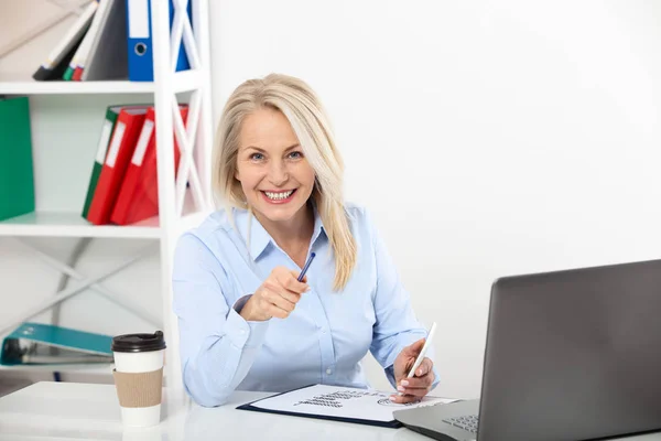 Mujer de negocios trabajando en la oficina con documentos. Hermosa mujer de mediana edad mirando a la cámara con sonrisa mientras se sienta en la oficina . — Foto de Stock