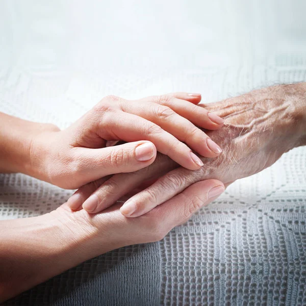 Old and young holding hands on light background, closeup. Care is at home of elderly — Stock Photo, Image