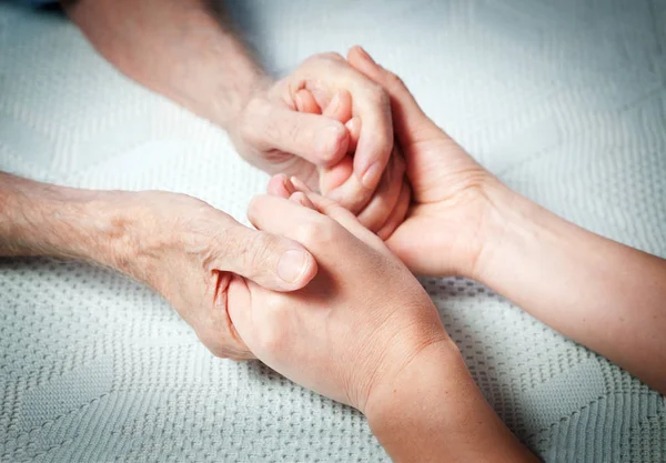 Old and young holding hands on light background, closeup. Care is at home of elderly — Stock Photo, Image
