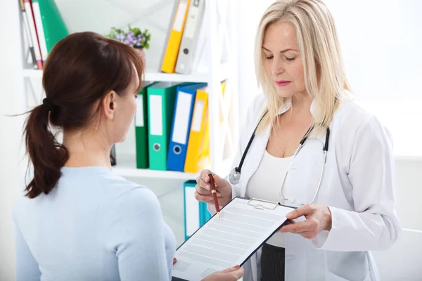 Médico femenino sosteniendo formulario de solicitud mientras consulta al paciente — Foto de Stock