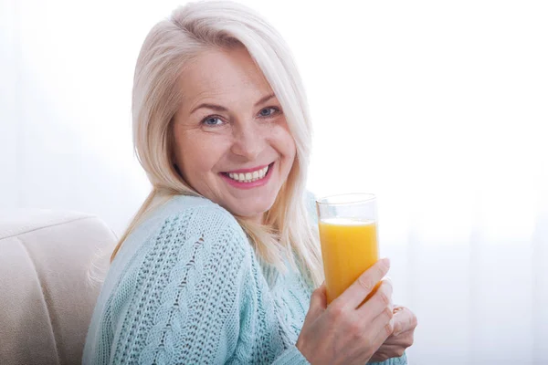 Mujer bebiendo jugo de naranja sonriendo. Hermosa mediana edad modelo caucásico cara primer plano . — Foto de Stock