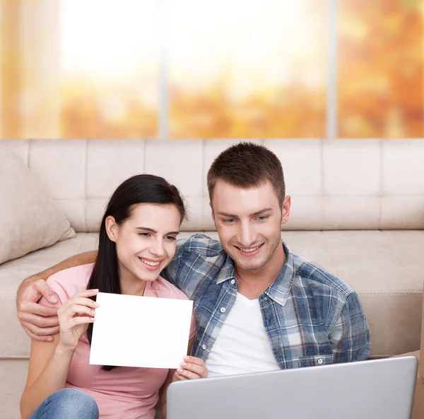 Όμορφο νεαρό ζευγάρι χρησιμοποιώντας φορητό υπολογιστή επικοινωνεί στη συνομιλία μέσω βίντεο. Μια γυναίκα είναι χαμογελώντας και δείχνοντας κενό κομμάτι του χαρτί. — Φωτογραφία Αρχείου