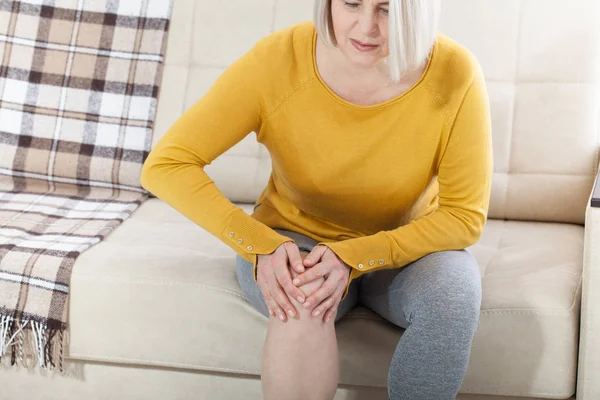 Frau mittleren Alters, die zu Hause unter Schmerzen im Bein leidet, Nahaufnahme. Körperverletzungskonzept. — Stockfoto