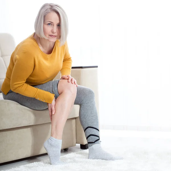 Frau mittleren Alters, die zu Hause unter Schmerzen im Bein leidet, Nahaufnahme. Körperverletzungskonzept. — Stockfoto