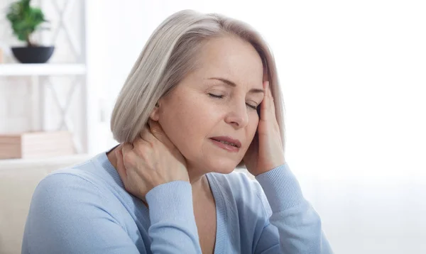 Woman suffering from stress or a headache grimacing in pain as she holds the back of her neck with her other hand to her temple, with copyspace. Concept photo with indicating location of pain. — Stock Photo, Image