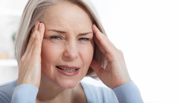 Frau, die unter Stress oder Kopfschmerzen leidet, grimmig vor Schmerzen, während sie den Nacken mit der anderen Hand an die Schläfe hält, mit Kopierplatz. Konzeptfoto mit Angabe der Schmerzstelle. — Stockfoto