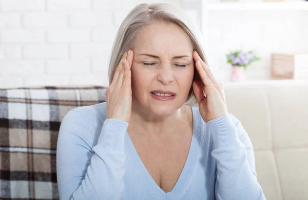 Woman suffering from stress or a headache grimacing in pain as she holds the back of her neck with her other hand to her temple, with copyspace. Concept photo with indicating location of pain. — Stockfoto