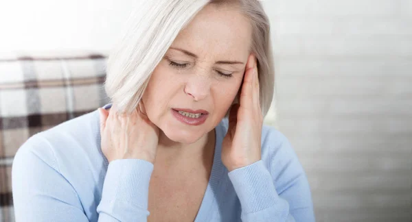 Frau, die unter Stress oder Kopfschmerzen leidet, grimmig vor Schmerzen, während sie den Nacken mit der anderen Hand an die Schläfe hält, mit Kopierplatz. Konzeptfoto mit Angabe der Schmerzstelle. — Stockfoto