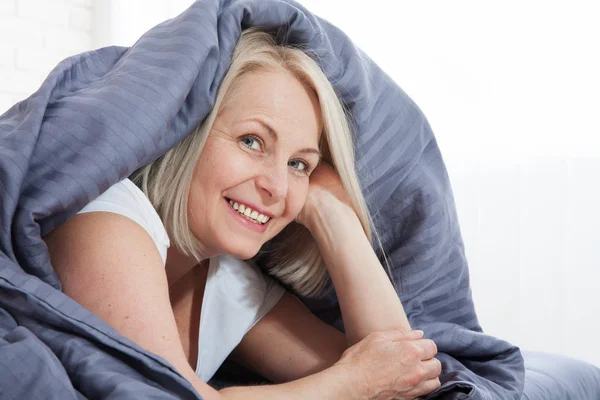 Happy woman hiding under the duvet in bed — Stok fotoğraf