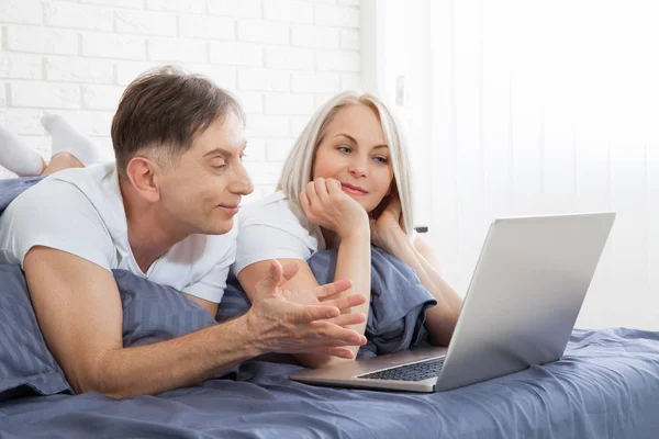 这对可爱的夫妇在卧室里用笔记本电脑在床上放松一下 — 图库照片
