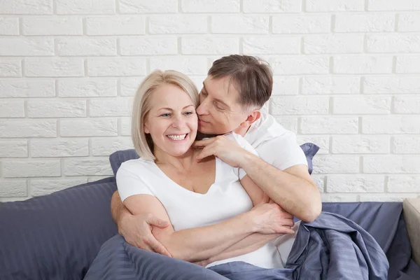 Bonito homem e mulher atraente estão gostando de passar o tempo juntos enquanto gentilmente abraçando e beijando sentado na cama . — Fotografia de Stock