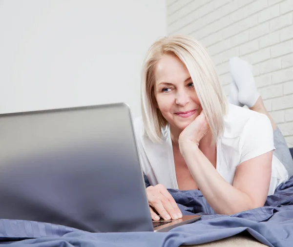 Mujer usando portátil en el dormitorio de casa. Un tipo acostado en la cama y escribiendo con una computadora portátil. Persona en la mañana con un dispositivo moderno, la lectura de correos electrónicos, el envío de mensajes. Concepto de teletrabajo — Foto de Stock