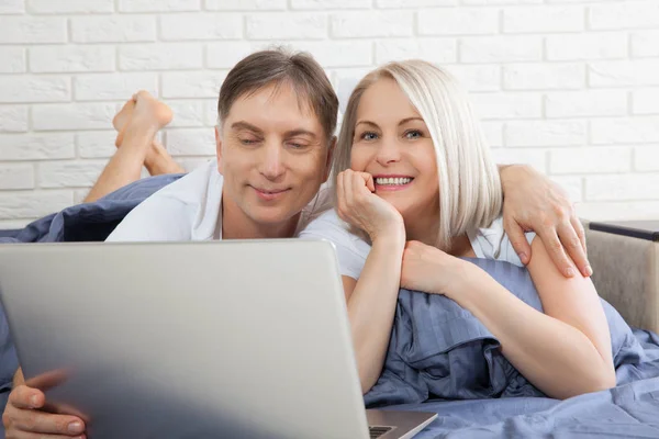 Piękna para amorów korzystająca z laptopa, na łóżku. Piękna kobieta i przystojny mężczyzna czytają wiadomości w Internecie. Związek pojęciowy. — Zdjęcie stockowe