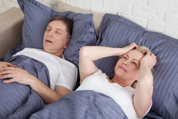 Snoring man. Couple in bed, man snoring and woman can not sleep. Middle age couple in bed at home. — 图库照片
