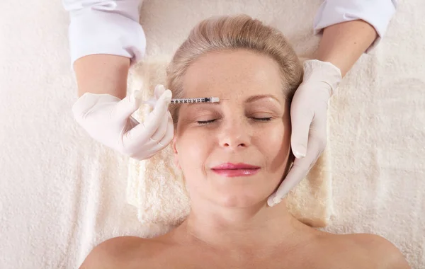 Mujer de mediana edad recibe inyección cosmética en la frente. Inyección de ácido hialurónico para rejuvenecimiento facial. Mujer en el salón de belleza. Clínica de cirugía estética . — Foto de Stock