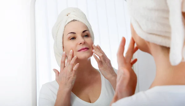 Mujer de mediana edad mirando las arrugas en el espejo. Cirugía plástica e inyecciones de colágeno. Maquillaje. Cara de macro. Enfoque selectivo en la cara . — Foto de Stock