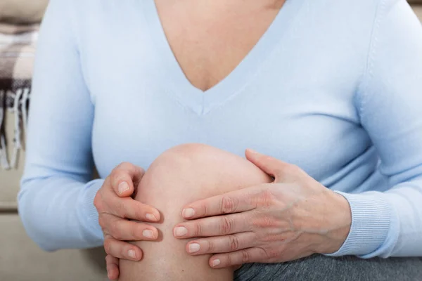 Frau mittleren Alters, die zu Hause unter Schmerzen im Bein leidet, Nahaufnahme. Körperverletzungskonzept. — Stockfoto