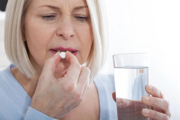 Doubtful sick ill middle woman holding pill and glass of water taking painkiller medicine drugs to relieve headache pain, worried about side effects of antidepressant or emergency contraceptive meds — Stock Photo, Image