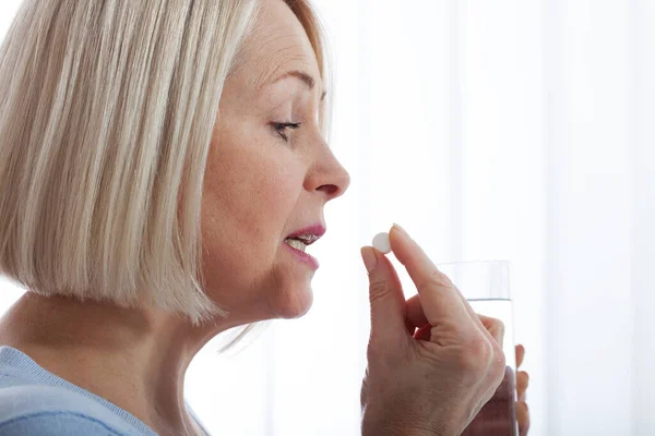 Middle woman feel unwell holding glass of water and pill doubting to take medicine. Exhausted female suffer from migraine or headache ready to have antibiotic or painkiller. — Stock Photo, Image