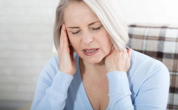 Frau, die unter Stress oder Kopfschmerzen leidet, grimmig vor Schmerzen, während sie den Nacken mit der anderen Hand an die Schläfe hält, mit Kopierplatz. Konzeptfoto mit Angabe der Schmerzstelle. — Stockfoto