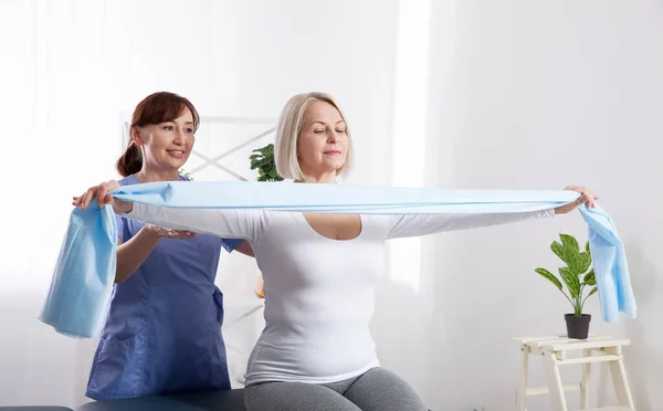 Fisioterapeuta y mujer sentados en una cama haciendo ejercicio con una cinta de goma — Foto de Stock