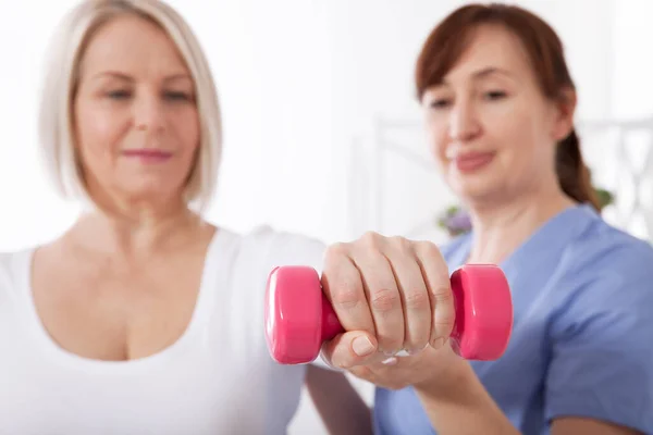 Moderne Reha-Physiotherapie. Physiotherapeutin hilft einer Frau mittleren Alters, sich durch Übungen mit Hanteln von einer Verletzung zu erholen. — Stockfoto