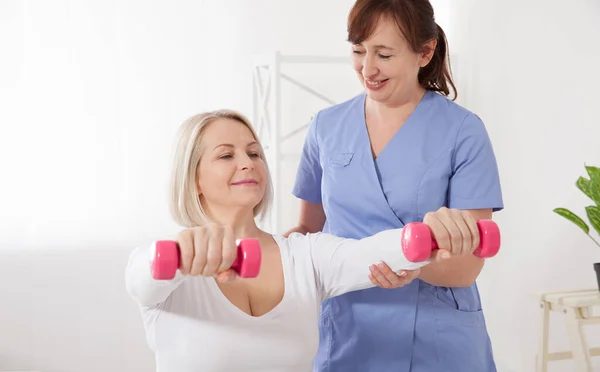 Picture of middle aged woman during rehabilitation in professional clinic. Rehabilitation, physiotherapy with dumbbells — Stockfoto