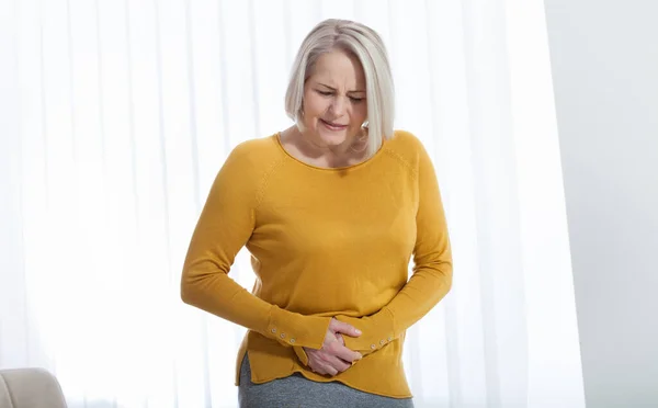 Donna di mezza età che soffre di dolore addominale mentre è a casa — Foto Stock