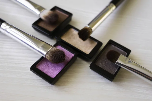 Close up on four eye shadows and makeup brushes.
