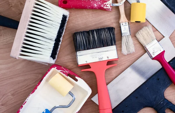 Paint brushes, rollers and putty knifes on a wooden background. A pile of used renovation tools.