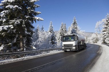 Tanker karla kaplı ağaçlar arasında bir asfalt yolda. Doğada kış.