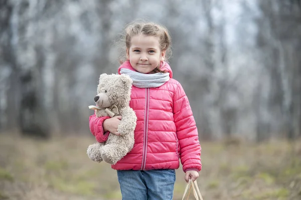 Очаровательная молодая девушка с радостью держит в руках упакованную коробку с подарком. Ребенок держит плюшевого мишку в руке на фоне дикой природы в весеннюю теплую погоду на прогулке в лесном парке — стоковое фото
