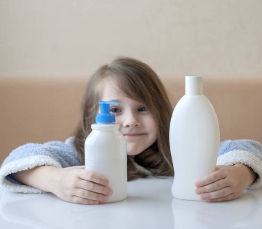 Kameraya bakarak farklı beyaz güzellik tuvalet malzemeleri onun elinde tutmak sevimli küçük kız. Bebek banyo, hijyen aksesuar. Kozmetik ürünleri kümesi. Köpükler, şampuan için kozmetik paket koleksiyonu