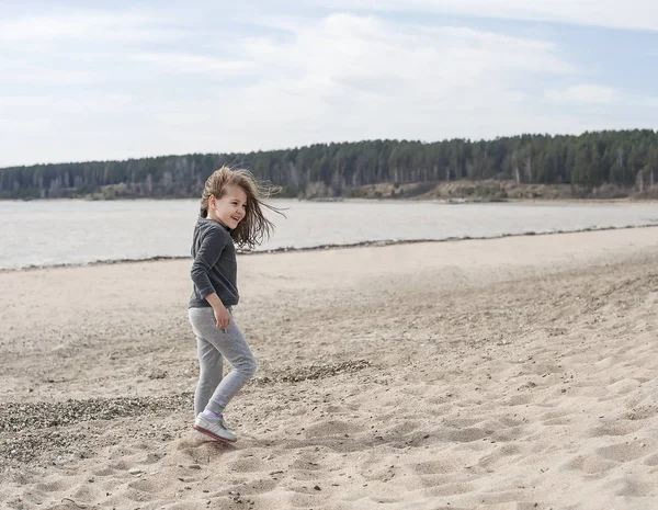 Kleines süßes Mädchen mit braunen langen Haaren, das an einem bewölkten Tag am Strand läuft. Urlaub am Meer — Stockfoto