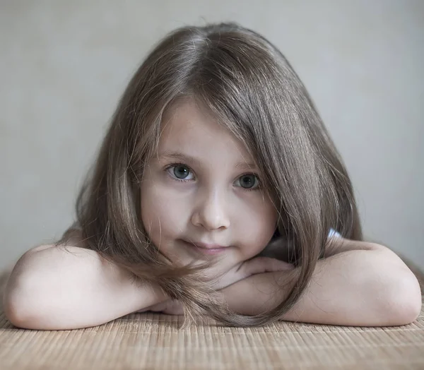 Uma garotinha sorrindo está sentada na mesa, olhando para a câmera. Retrato emocional. Curiosidade, impulso, energia, entusiasmo, indagação, interesse, alegria, riso, amoroso, travessura, prazer, ternura — Fotografia de Stock