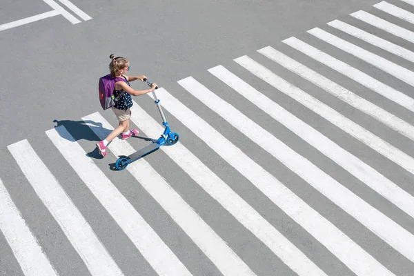 Menina carregando scooter e cruzando estrada a caminho da escola — Fotografia de Stock