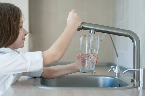 Grifo de la cocina. Lindo niño rizado vertiendo agua dulce del grifo del filtro. En interiores. Concepto de vida saludable —  Fotos de Stock