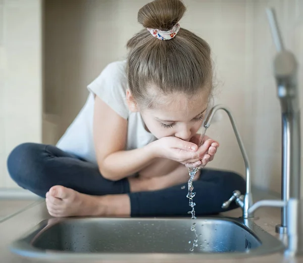 Caucasian cute girl is drinking from water tap or faucet