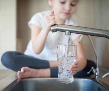 Little girl opens a water tap with her hand holding a glass