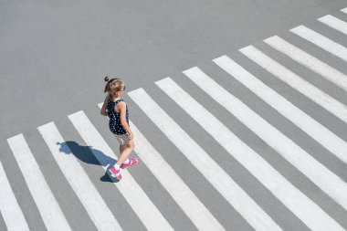 Güneş gözlüklü şık bir çocuk, yaz kenti yaya geçidinde yürüyen moda kıyafetleri. Yaya kaldırımında yürüyen bir çocuk. Yaya geçidinden geçen yayalar. Yukarıdan bakınca. Arkasında. Zebra geçidindeki gölge