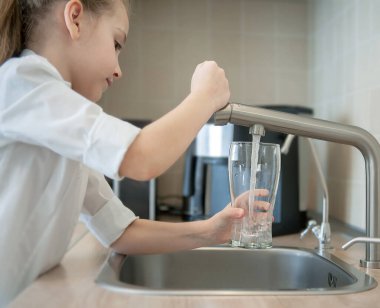 Portrait of little caucasian girl gaining a glass of tap clean water. Kitchen faucet. Kid pouring fresh water from filter tap. Concept nature, purification, freshness. Healthy drink for healthy life