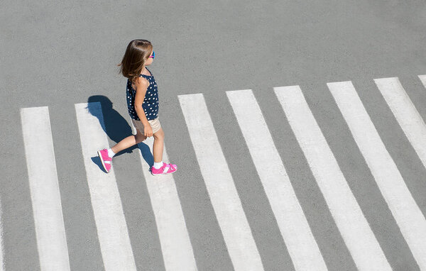 Stylish child in fashion clothes is walking along summer city crosswalk. Kid on pedestrian side walk. Concept pedestrians passing a crosswalk. Traffic rules. From top view. Shadow at zebra crossing