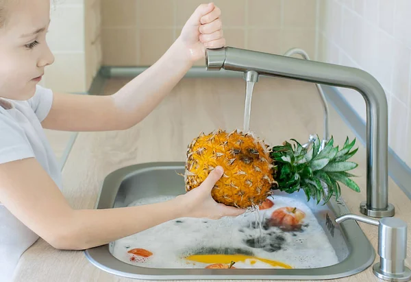 Child washing fresh pineapple in running water in kitchen sink. Sanitizing fruits and vegetables before eating. Hygiene concept. Disinfection of products from store. Coronavirus infection prevention