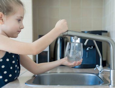 Çocuğun elinde şeffaf bir cam var. Bardak içeceği dolduruyorum. Taze içki dolduruyorum. Musluk suyu tüketimi plastik şişelerde suyun korunmasına ve çevrenin korunmasına katkıda bulunur.